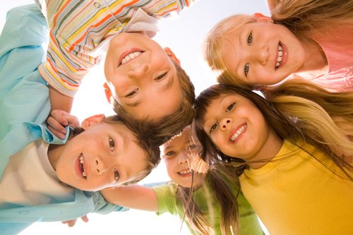 Below view of happy children embracing each other and smiling at camera