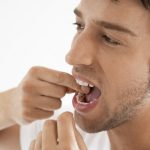 Man flossing his teeth with a white background.