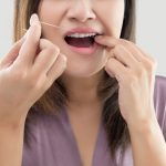 Woman flossing teeth in a purple robe.